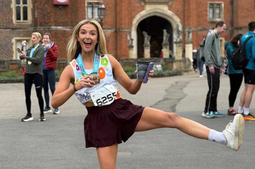 RMCC runner smiling at the camera and holding her medal up sticking her leg in the air