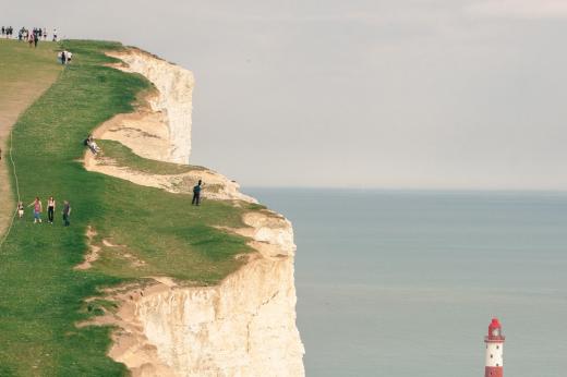 RMCC trekkers in the distance on a cliff doing the south downs trek with a lighthouse to the right 