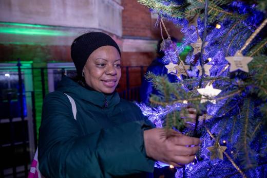 Debbie, wearing a black hat and green jacket looks at gold star decorations on a Christmas tree