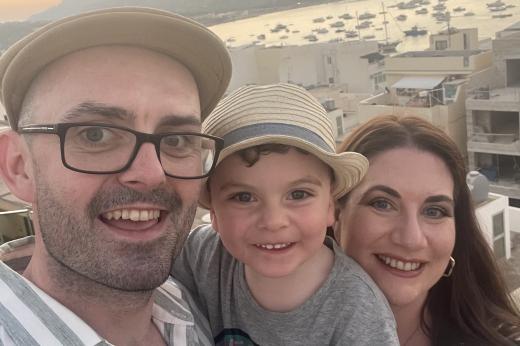 Tash smiling with her husband and son near a harbour during sunset