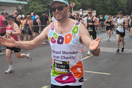 RMCC runner running past the camera smiling with his arms and hands open with runners and supporters in the background. 