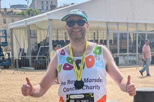RMCC runner with medal round his neck and thumbs up smiling to the camera with the London Eye in the background. 