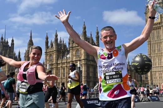 RMCC runner and his daughter smiling with their arms in the air as they run through London with Big Ben and other runners in the background. 