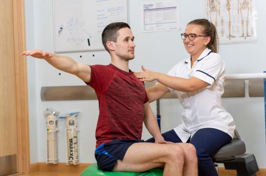 A man sitting on a ball and a nurse helping with his posture