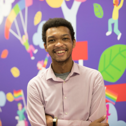 Joshua, member of the Youth Forum standing in front of the colourful mural smiling