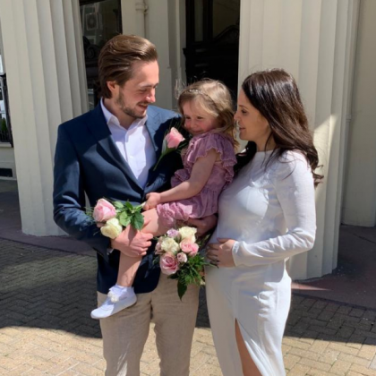 Photo of Thomas smiling. He is holding his young daughter and beside his wife 