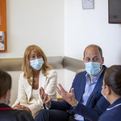 3 women and one man sit talking. The man is HRH The Duke of Cambridge. All are wearing surgical masks