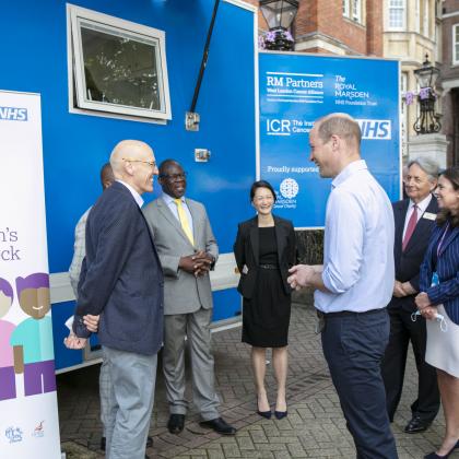 Group of people stood talking outside a van. One of the men is HRH The Duke of Cambridge