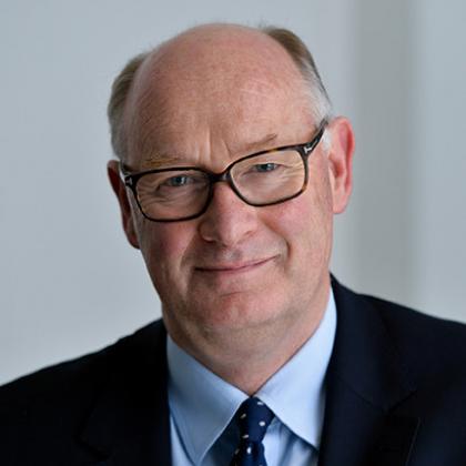 Sir Douglas Flint CBE, wearing a blue shirt and tie, and black rimmed glasses