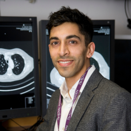 Dr Sumeet Hindocha smiling, sat infront of screens showing scans