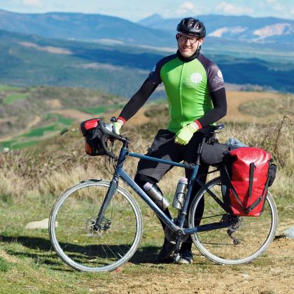 chris in a green Royal Marsden Cancer Charity cycling shirt with his bike in-front of a mountain landscape