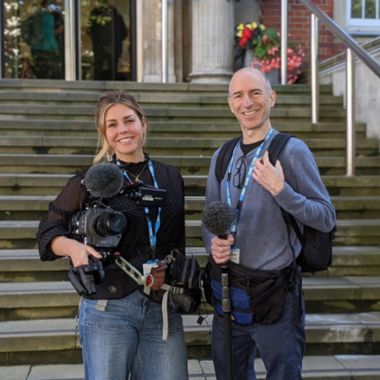 A mand and a woman holding a film camera and microphone on the steps of The Royal Marsden in Chelsea