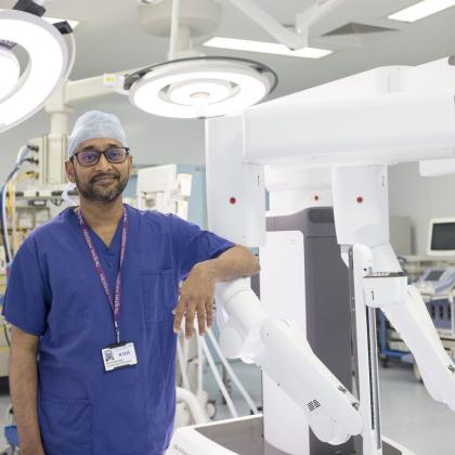 Professor Vinidh Paleri with the Da Vinci Xi robot. He is wearing blue scrubs and a cap.