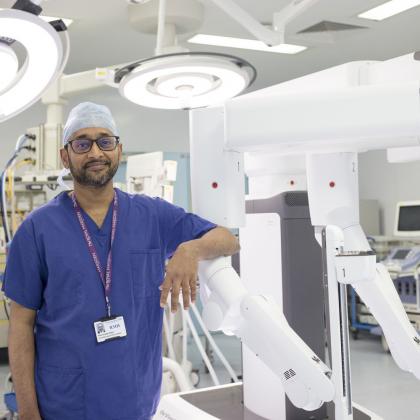 Professor Vinidh Paleri with the Da Vinci Xi robot. He is wearing blue scrubs and a cap. 