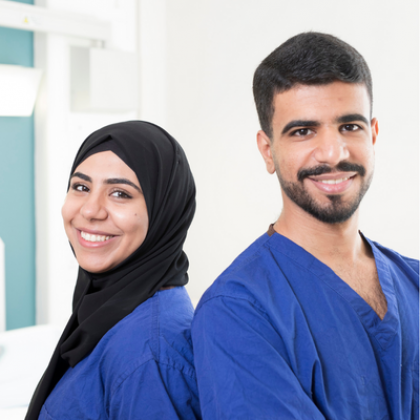 Sara (left) and Abed (Right) standing back to back. They are smiling and wearing blue scrubs. Sara is wearing a Hijab