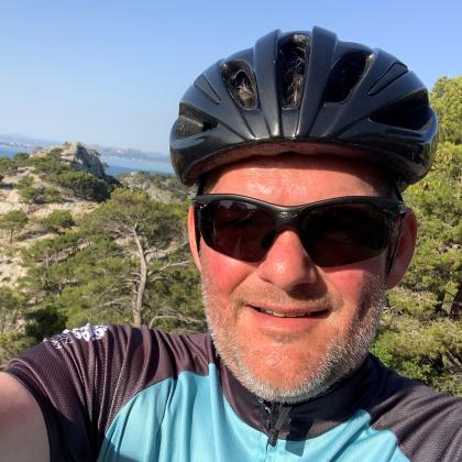 Selfie of Nick van As. He is wearing a black cycling helmet and sunglasses and a blue and grey cycling jersey. 