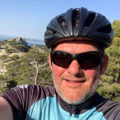 Selfie of Nick van As. He is wearing a black cycling helmet and sunglasses and a blue and grey cycling jersey.