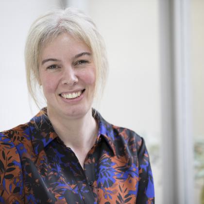 Dr Anna Minchom smiling. She has blonde hair and is wearing a red and blue patterned shirt