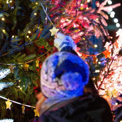 A photo of a lady in a knitted hat looking at a Star on the Christmas Tree