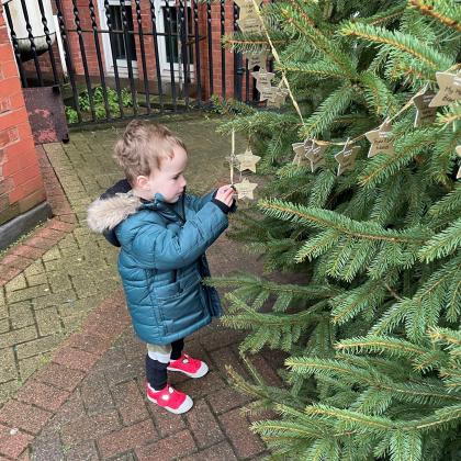 3 year old Dexter looking at Stars on the Celebrate a Life Christmas Tree. He is in a blue winter coat and red shoes. 