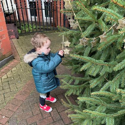 3 year old Dexter looking at Stars on the Celebrate a Life Christmas Tree. He is in a blue winter coat and red shoes.