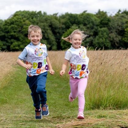 Reece and Emilie running in a field. They are wearing colourful Royal Marsden Cancer Charity running bibs