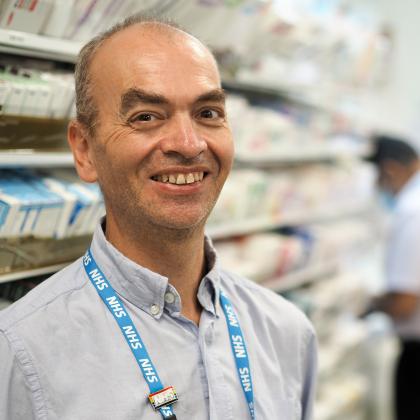 Photo of Rob in the Pharmacy at The Royal Marsden. He is smiling and wearing a blue shirt and NHS lanyard