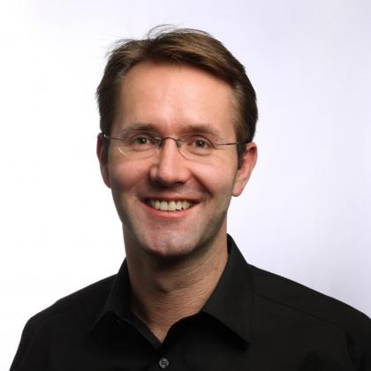 Portrait photo of Andrew Fisher. He is wearing a black shirt and glasses and is smiling. 