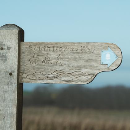 A close up photo of a South Downs Way signpost with the landscape blurred in the background