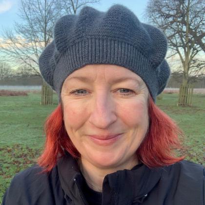 A photo of Pip smiling. She has A grey knitted hat on and bright red hair.