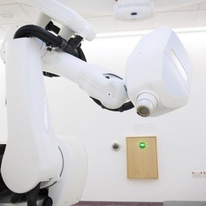 A large white machinbe that resembles a robotic arm leaning over a flat surface for a patient to lie on.