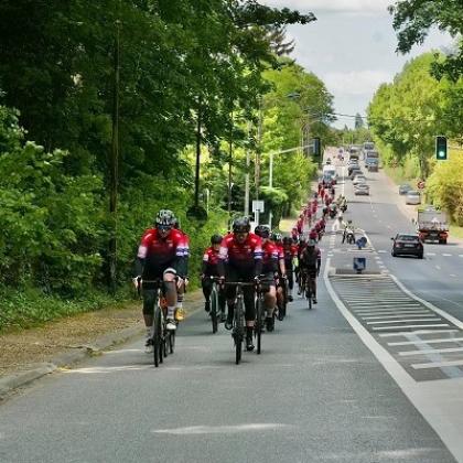 A long line of cyclists biking on a busy suburban road