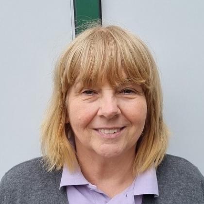 Head and shoulders of a woman with short blonde hair with a fringe, wearing a collared shirt and a cardigan