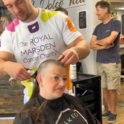 Lea sitting in a hairdresser chair with a person in a Royal Marsden Cancer Charity t-shirt shaving her head