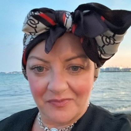 Head and shoulders shot of Lea in a headscarf in front of the sea