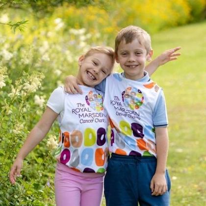Two young children in a flowery park, smiling with their arms around each other and wearing RMCC t-shirts