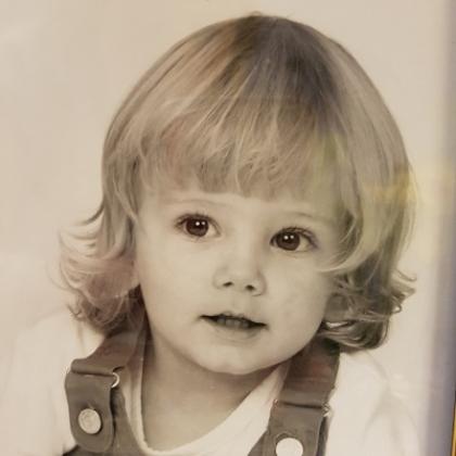 A black and white image of a small child with short light hair and wearing dungarees