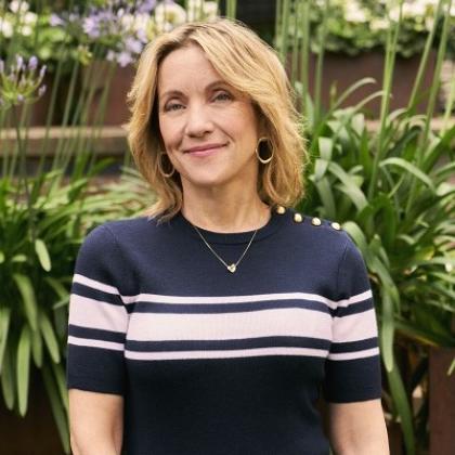 A Royal Marsden with short blonde hair, and a pink and navy striped top standing in a garden