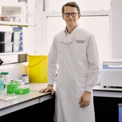 A Royal Marsden doctor in a long white coat standing in a medical room with test tubes and equipment on the counters