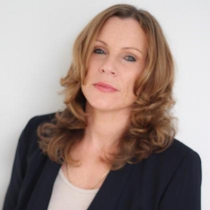 A headshot of a woman with curled blonde hair wearing a a cream top and black blazer