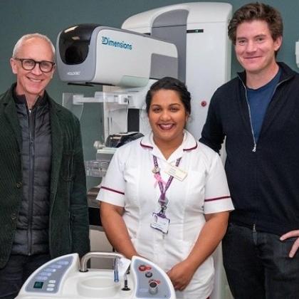 Three people, including a Royal Marsden Radiographer in uniform in the middle, standing in front of a large piece of white machinery in a hospital room