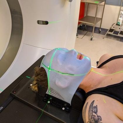 A person lying down underneath a scanner with a mesh-like mask over their face