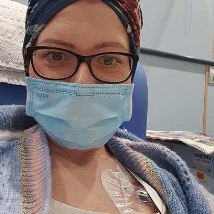 Aneta receiving chemotherapy through her port at The Royal Marsden. She's wearing a hair wrap, knitted cardigan and face mask