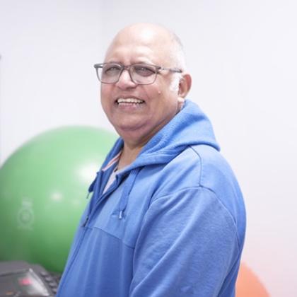 Upper half of Naz. He is wearing a blue hoodie and smiling, with a green exercise ball behind him.