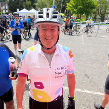 Torso of Francis in white Charity shirt and grey cycle helmet. Other cyclists are in the background.