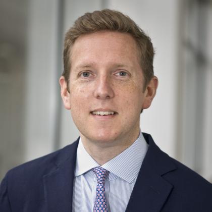 A headshot of Dr Andrew Furness. Image of a smiling young man in a dark suit and tie. 