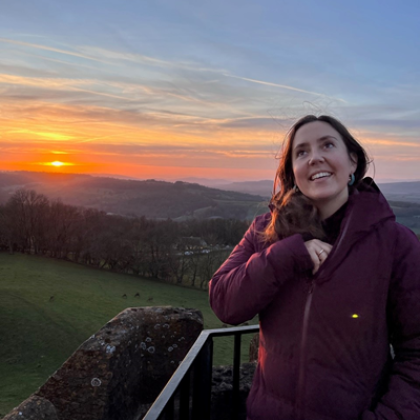 Tabitha standing in front of a sunset, looking up at the sky, wearing a purple jacket