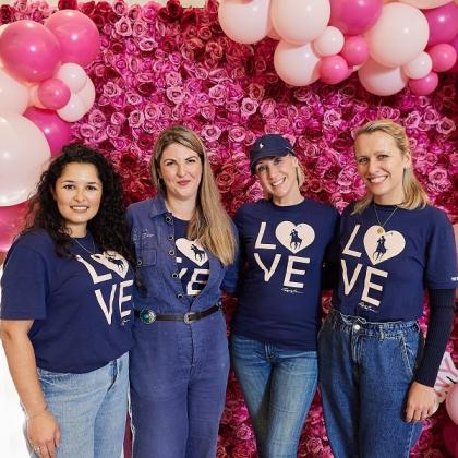 Four people in blue Ralph Lauren LOVE shirts smiling and standing in front of a bright pink wall decorated with flowers and balloons
