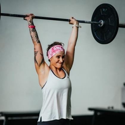 Fran in gym gear lifting up a heavy weight over her head