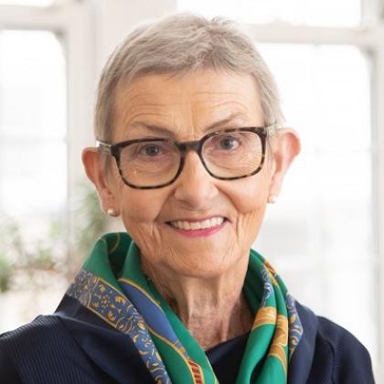Head and shoulders of a woman with short grey hair, she's smiling and wearing stylish glasses and dark blue and green scarf